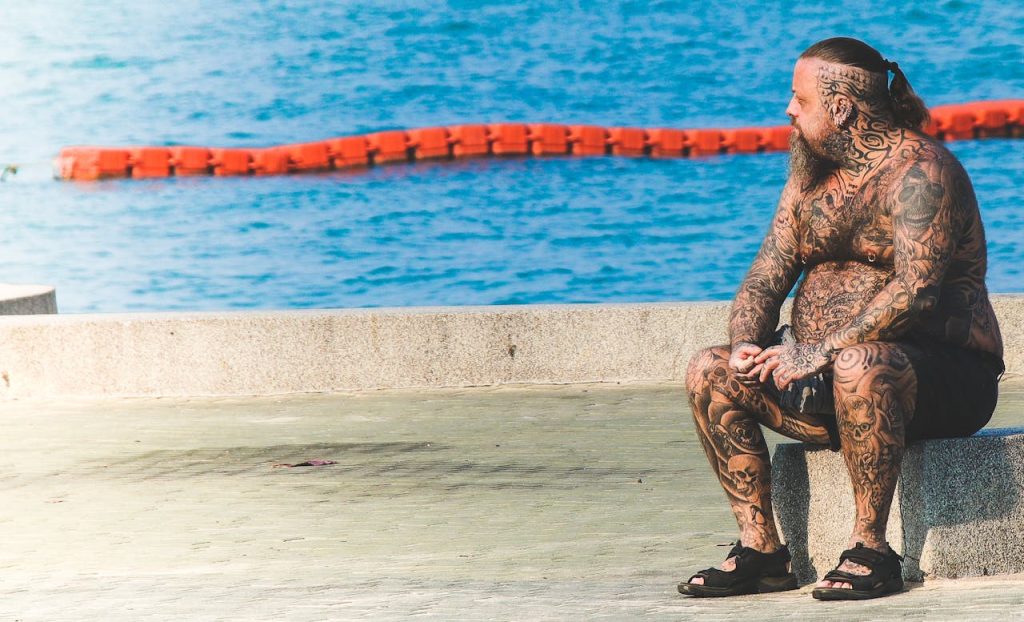 heavily tattooed man sitting by the swimming pool