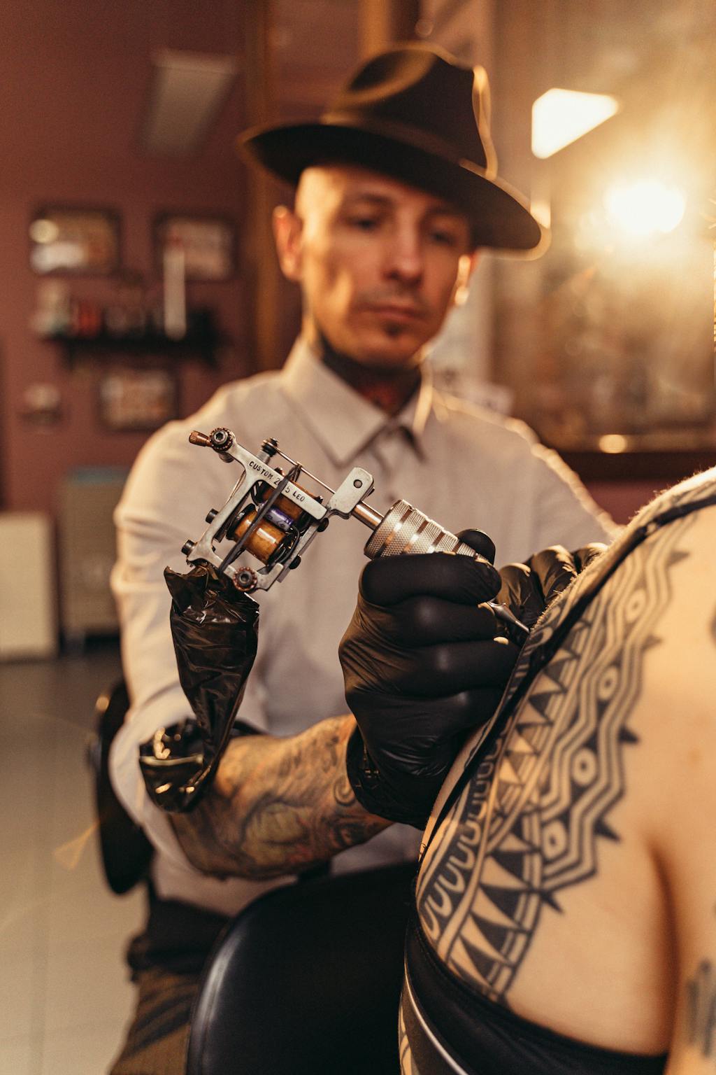 Professional tattoo artist wearing black gloves and using a tattoo machine on a client in a clean studio setting